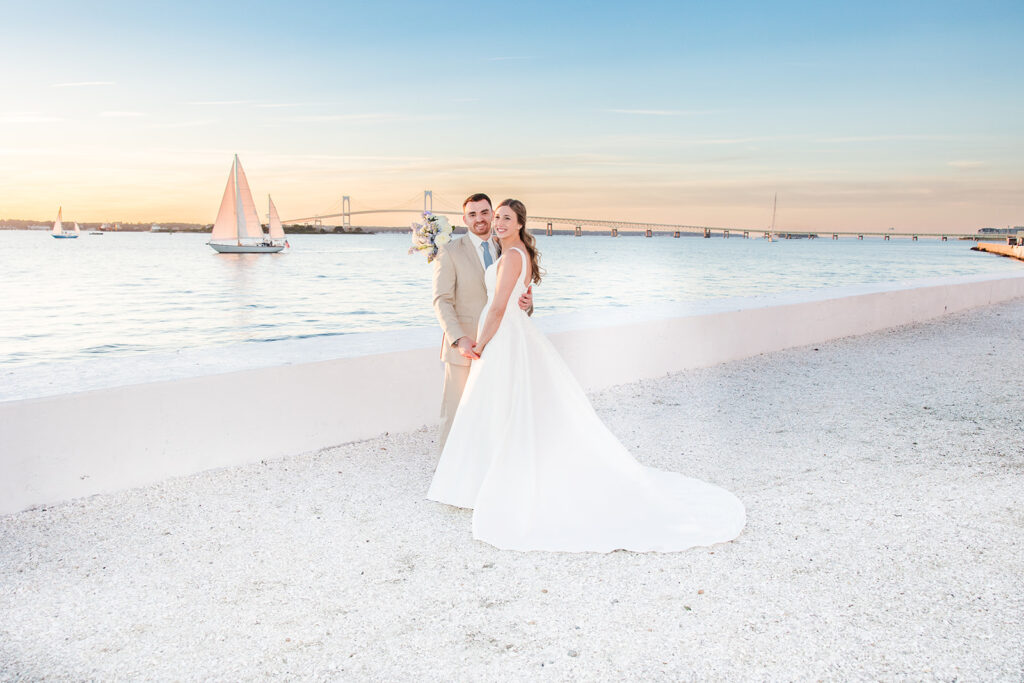 Bride and groom kissing at sunset along the waterfront at Belle Mer in Newport, Rhode Island with the Claiborne Pell Bridge in the background.