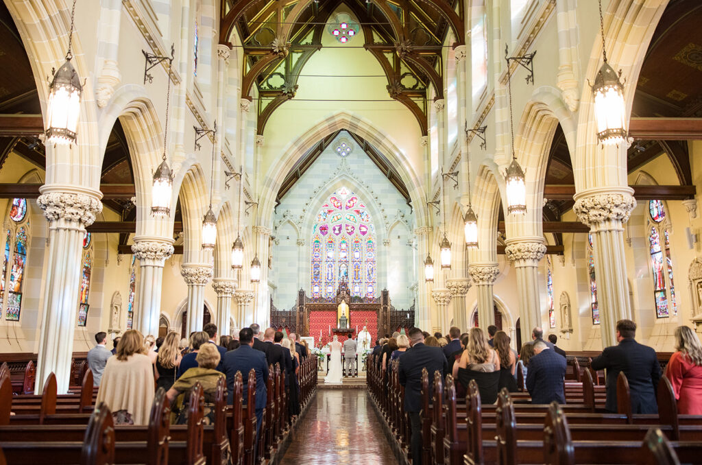 Wedding ceremony at St. Mary’s Church in Newport Rhode Island with stained glass altar and guests seated in pews