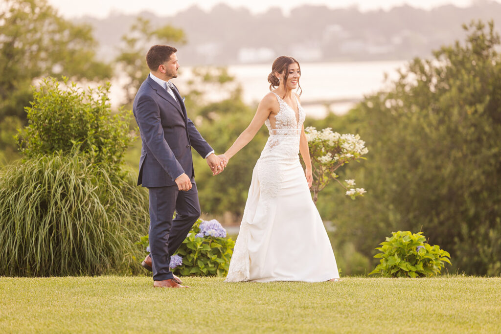 Bride and groom walking hand in hand at sunset on the lawn at Wyndham Newport Hotel in Middletown, Rhode Island.