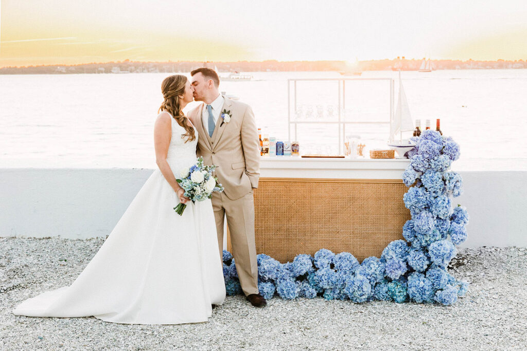 Bride and groom portrait on Belle Mer’s waterfront terrace with blue floral installation overlooking Narragansett Bay