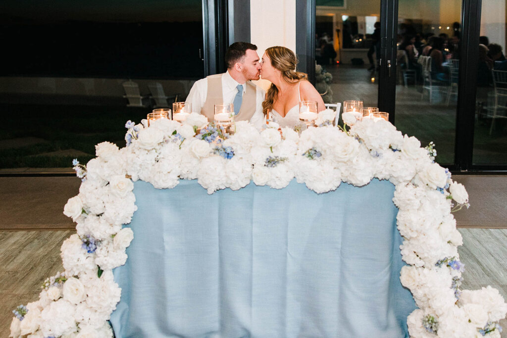Bride and groom kiss at sweetheart table during Belle Mer wedding reception
