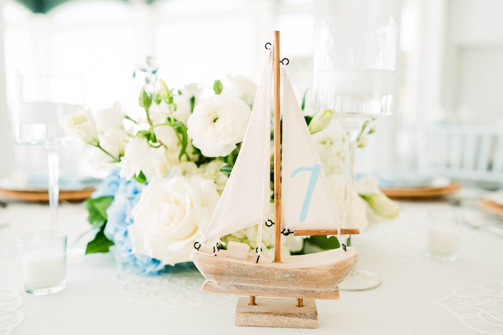 Coastal-inspired tablescape details with florals and sailboat accents at Belle Mer reception
