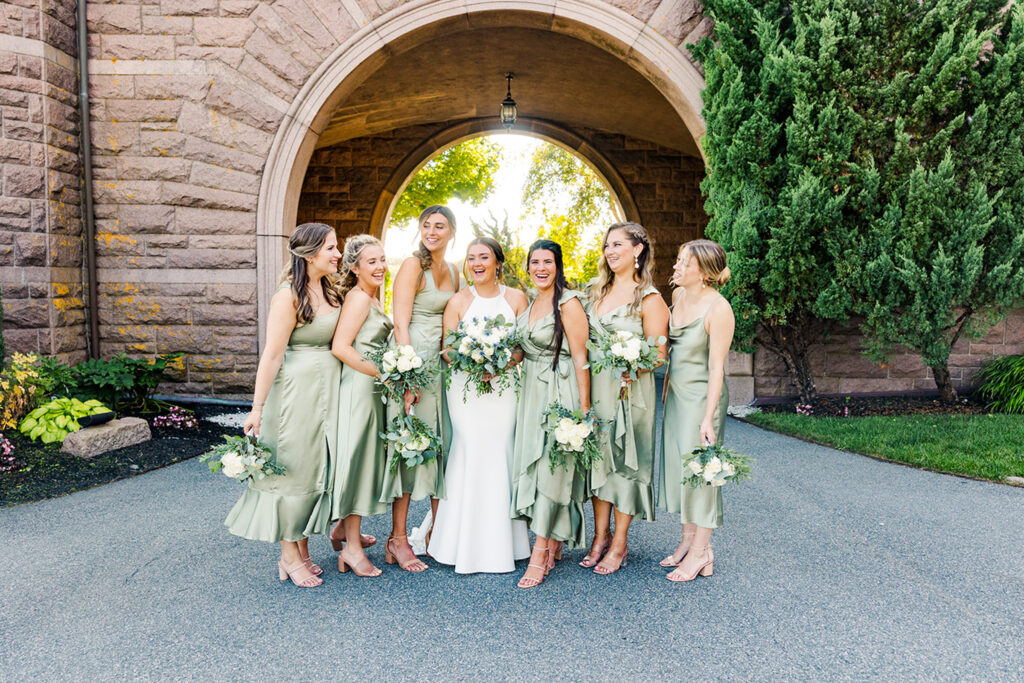 Bride and bridesmaids posing beneath the stone arch at OceanCliff