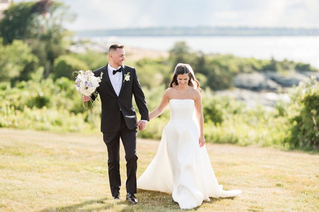 Bride and groom walking across the waterfront lawn at OceanCliff in Newport