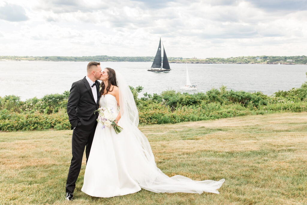 Bride and groom with a sailboat and Narragansett Bay behind them at OceanCliff